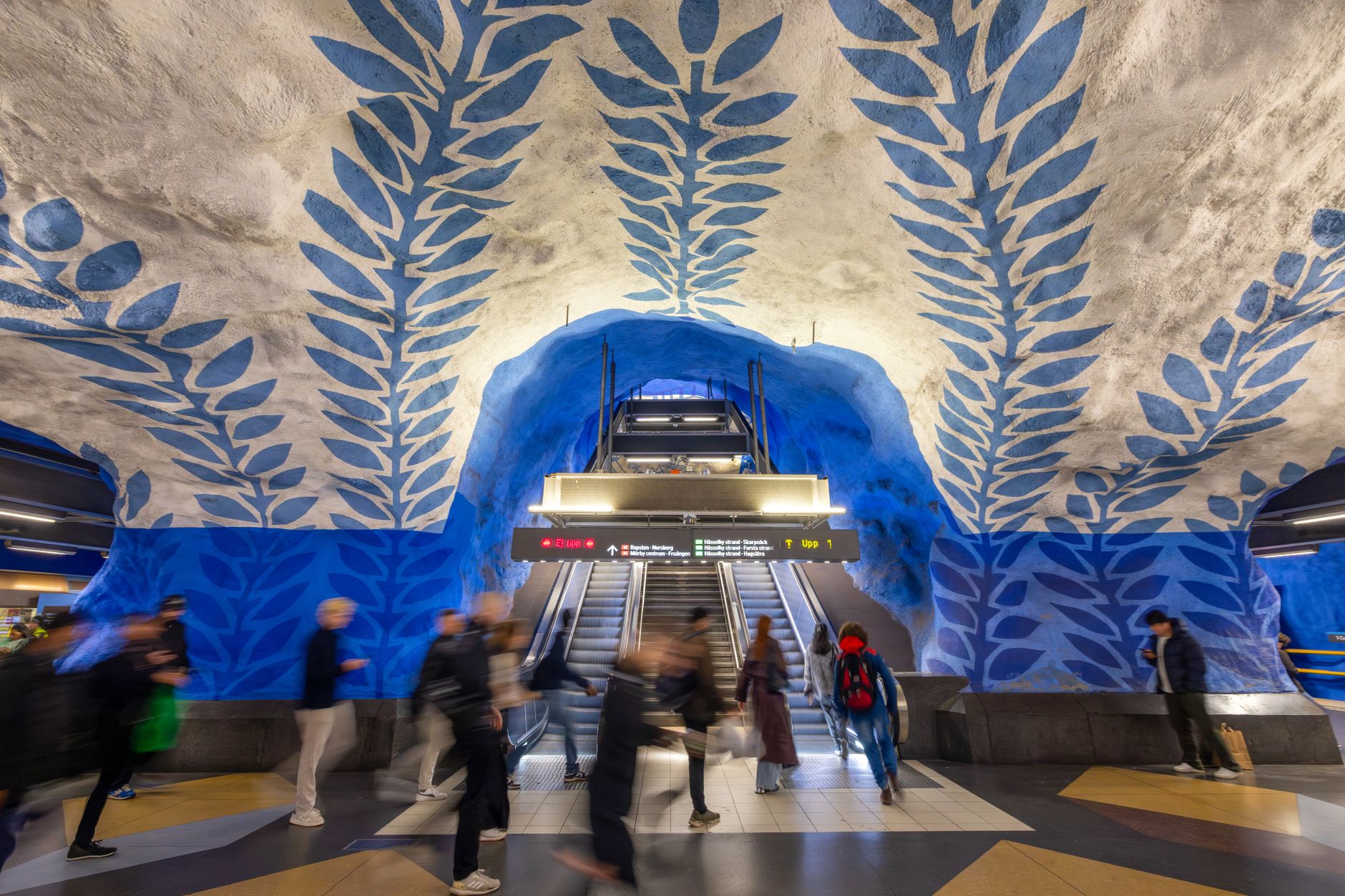 Blurred motion of people at an artistic Stockholm metro station with blue leaf ceiling. — illustrating How Does the Stockholm Travel Card Work Across Transport?