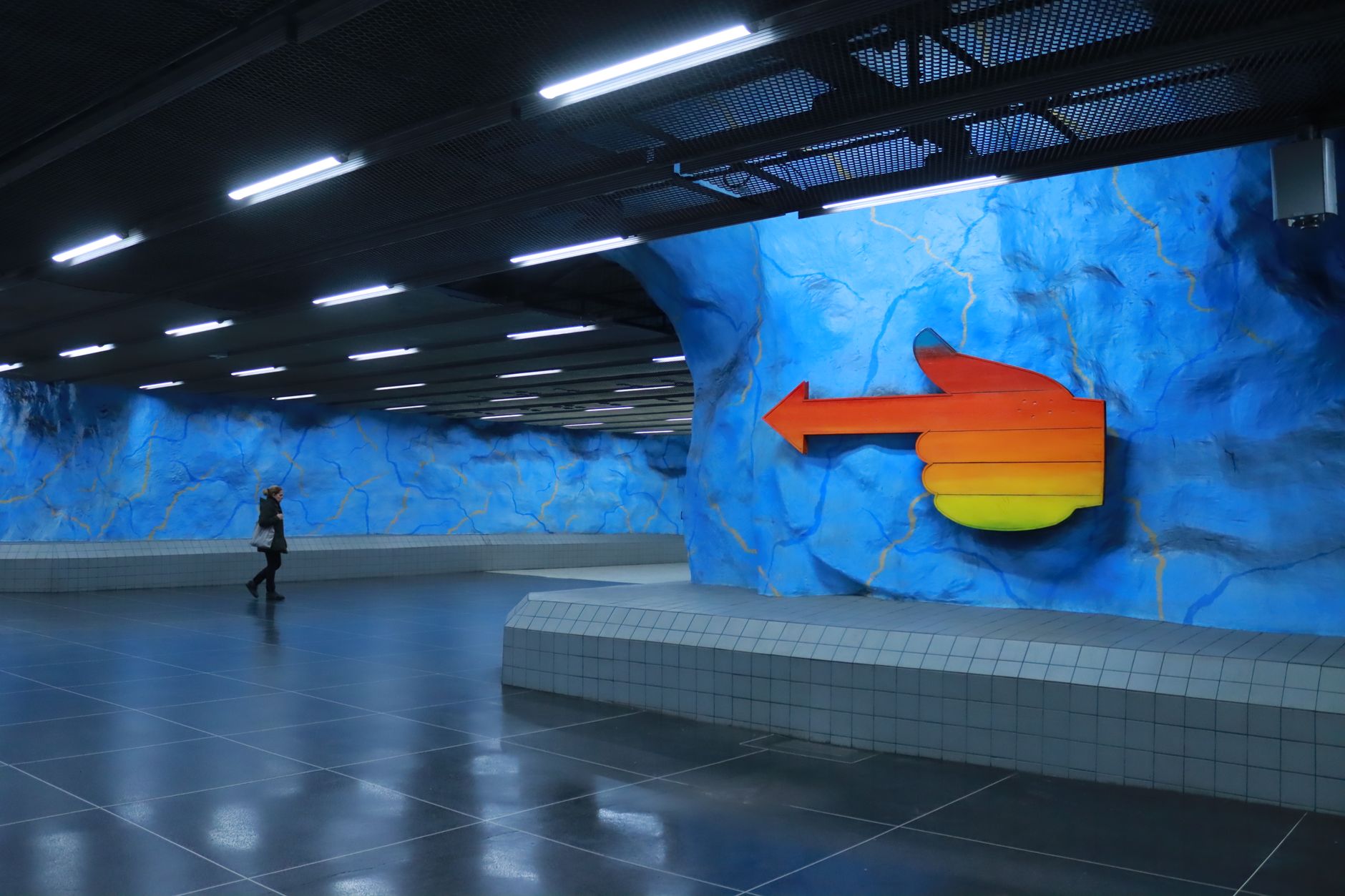 Vibrant blue walls and arrow sign in Stockholm's Stadion metro station.